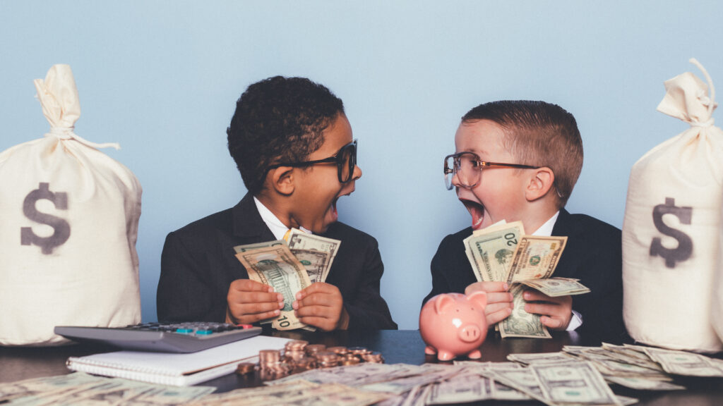 Two kids dressed like businessmen scream while holding handfuls of money next to two moneybags.