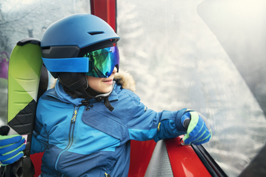 Little boy snowboarding with on a sunny winter day. The boy is looking at view in gondola ski lift ride.